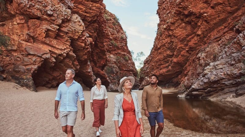 Four adventurers marvel at dramatic red cliffs and a crystal-clear pool on a 1 Day West MacDonnell Ranges tour with Standley Chasm.
