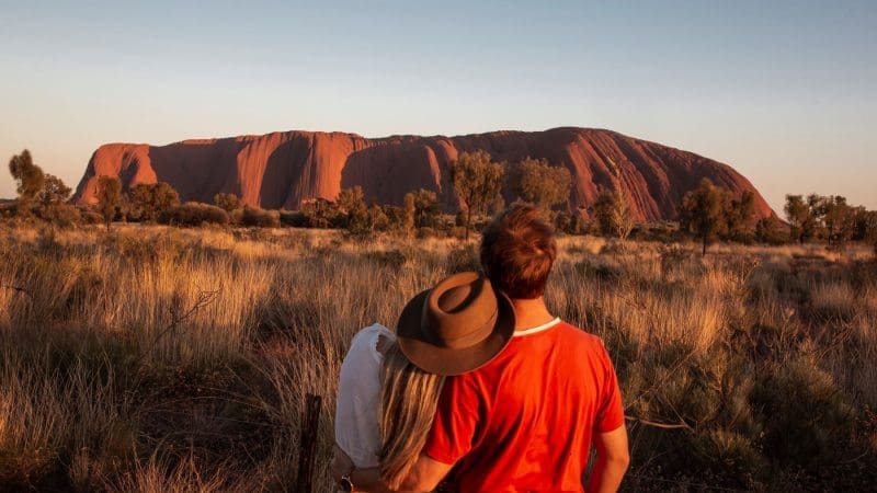 Couple gazes at Uluru during a stunning sunset on a 7-day Adelaide to Uluru Adventure by Untamed Escapes, Australia tour.
