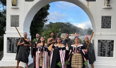 Eight performers in vibrant traditional Māori dress pose beneath a white archway after a Whakarewarewa Cultural Performance in New Zealand.