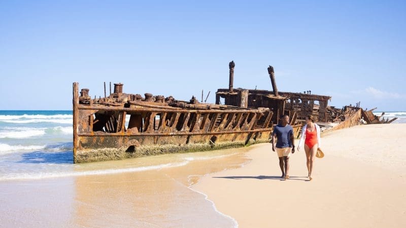 Couple walks by a rusty shipwreck during a 14-Day Sydney to Cairns tour with stops at Fraser Island and Whitsundays, Australia.