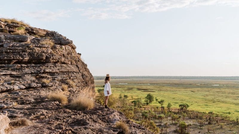 Traveller in white standing atop a rugged cliff, overlooking lush green plains—ideal for an unforgettable 1 Day Kakadu Wilderness tour.